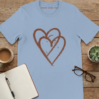 Load image into Gallery viewer, Light Blue self-care graphic t-shirt flat lay with notebook and glasses.