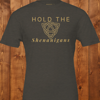 Load image into Gallery viewer, Flat lay mockup of the "Hold the Shenanigans" t-shirt in dark olive green with gold text and a Celtic knot.