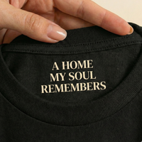 Load image into Gallery viewer, Detailed view of the inner neck printing on the 'Inner Anchor' t-shirt. Features the soulful quote "A HOME MY SOUL REMEMBERS" in elegant gold serif font on sensory-friendly sueded cotton.