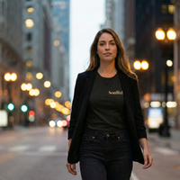 Load image into Gallery viewer, Professional woman walking through city lights at night wearing a tailored blazer over the 'Inner Anchor' premium sueded cotton tee in Black. Features the minimalist 'Soulful' serif typography.
