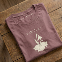 Load image into Gallery viewer, "Folded mauve Bella Canvas 3001 t-shirt on wood background featuring Yukidoke The Thaw design. Soft cotton emotional support clothing."