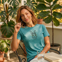 Load image into Gallery viewer, A woman relaxing in a sunlit plant conservatory wearing a heather teal premium luxury tee with a vintage-inspired rabbit and gold glasses graphic.