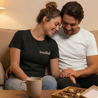 Load image into Gallery viewer, Couple sitting on a couch wearing matching "Soulful" t-shirts in Black and White. Romantic lifestyle photography for relationship-themed apparel.