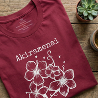 Load image into Gallery viewer, Cardinal red Akiramenai t-shirt flat lay on a wooden surface accented with small potted succulent plants for a wellness aesthetic.
