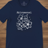 Load image into Gallery viewer, Navy blue Akiramenai graphic tee laid flat on a wooden table, highlighting the white floral design and Japanese text.