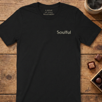 Load image into Gallery viewer, Vital Threads "Soulful" t-shirt in Black. Minimalist flat lay on a rustic wooden table with chocolates and coffee, featuring simple "Soulful" text on the left chest.
