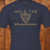 Load image into Gallery viewer, Flat lay mockup of the "Hold the Shenanigans" t-shirt in navy blue with gold text and a Celtic knot.