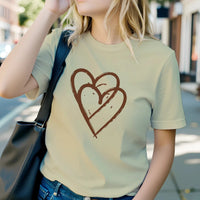 Load image into Gallery viewer, Woman wearing cream yellow t-shirt with large hand-drawn interlocking hearts graphic in rust brown. Soft, organic aesthetic.