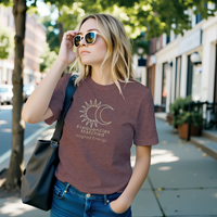 Load image into Gallery viewer, Woman walking on a city street wearing a heather mauve t-shirt with a gold "Frequencies Matched" Sun and Moon graphic. Spiritual streetwear aesthetic.