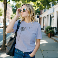 Load image into Gallery viewer, No. 25: The Emergence - Woman walking down a city street wearing a light grey premium luxury tee with a botanical dandelion graphic