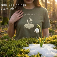 Load image into Gallery viewer, "Close up detail of botanical graphic tee showing a snowdrop flower growing from a melting heart. Self-care and mental health awareness fashion."