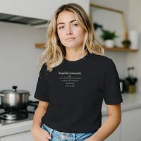 Load image into Gallery viewer, Blonde woman in a modern kitchen wearing the black 'Hopeful Romantic' sueded cotton tee. Minimalist wellness apparel for everyday comfort.