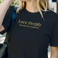 Load image into Gallery viewer, Blonde woman wearing black graphic tee with vintage gold serif text "Love Deeply Boundaried completely." standing in a modern kitchen. Quiet luxury aesthetic.