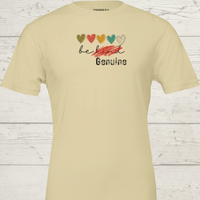 Load image into Gallery viewer, Bella and Canvas Natural Colored graphic tee featuring red scratch over 'Be Kind' text and distressed 'Genuine' logo."