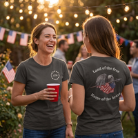 Load image into Gallery viewer, Two women at an evening backyard gathering wearing the Land of the Free, Home of the Brave shirt in Vintage Black — one showing the front 1776 star-circle badge, the other showing the back eagle and flag graphic with 'Land of the free' and 'Home of the brave' text.