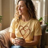 Load image into Gallery viewer, CWoman drinking coffee wearing a soft Bella Canvas 3001 t-shirt in yellow with heart design.