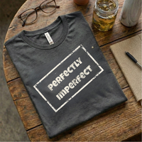 Load image into Gallery viewer, Alt Text: Dark Charcoal Grey t-shirt folded on a wooden table with glasses and iced coffee. Features the grunge "Perfectly Imperfect" graphic.