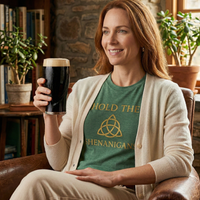 Load image into Gallery viewer, A smiling woman with auburn hair relaxing in a leather armchair, holding a dark beer. She is wearing an open cream cardigan over a heather green t-shirt featuring a gold Celtic knot and the text "Hold the Shenanigans.
