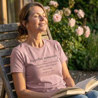 Load image into Gallery viewer, Woman sitting in a garden chair enjoying the sun, wearing the Mauve Vital Threads "Hopeful Romantic" tee and holding an open book. Represents a slow living lifestyle.