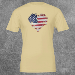 Flat lay of the Soft Cream Deep Roots, Steady Heart shirt on a grey textured background, showing the full distressed American flag heart graphic across the chest.