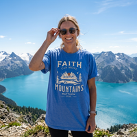Load image into Gallery viewer, Woman smiling at a turquoise mountain lake wearing the Heather Columbia Blue Faith can Move Mountains shirt.