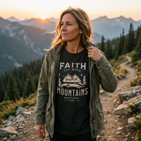 Load image into Gallery viewer, Woman standing on a mountain trail at sunset wearing the Vintage Black Faith can Move Mountains shirt under an open olive jacket.