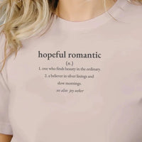 Load image into Gallery viewer, Close-up of the 'Hopeful Romantic' definition graphic on a women's premium sueded cotton tee in Dusty Mauve. Features minimalist typography describing one who finds beauty in the ordinary.