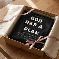 Load image into Gallery viewer, Black God Has A Plan t-shirt folded in a kraft gift box with cream tissue paper and dusty rose ribbon
