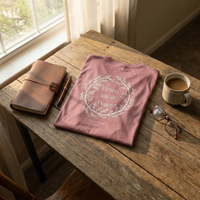 Load image into Gallery viewer, Flat lay on a rustic wooden table featuring two Heather Mauve No. 11 The Trilogy shirts, showcasing the front chest typography and back botanical wreath graphic.