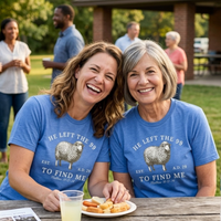 Load image into Gallery viewer, Two women laughing together at an outdoor gathering, both wearing the He Left the 99 to Find Me shirt in Heather Blue with the front sheep graphic visible.