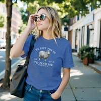Load image into Gallery viewer, Woman in sunglasses on a city sidewalk wearing the He Left the 99 to Find Me shirt in Heather Blue, front sheep graphic visible.