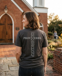 Load image into Gallery viewer, Woman standing outside a small-town brick church with a white steeple, seen from behind, wearing the Vintage Black He Will Straighten Your Path shirt with the Proverbs 3:5-6 back graphic visible.