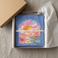 Load image into Gallery viewer, Folded Heather Columbia Blue His Mercies Are New Every Morning shirt displayed in an open kraft gift box with tissue paper and ribbon.