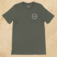 Load image into Gallery viewer, Front flat lay of the Land of the Free, Home of the Brave shirt in Heather Military Green, showing the 1776 star-circle badge and inner collar message at the neckline.