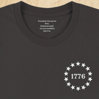 Load image into Gallery viewer, Collar detail of the Land of the Free, Home of the Brave shirt in Vintage Black, showing the hidden inner collar message ‘Freedom was never free. Someone paid so you wouldn't have to.’ above the front 1776 star-circle badge.