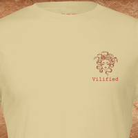 Load image into Gallery viewer, Close-up of Warm Cream shirt chest showing Medusa graphic and Vilified in red typewriter text