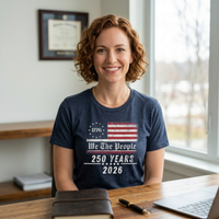 Load image into Gallery viewer, Confident female professional in a modern office wearing the distressed 1776 We The People graphic tee in Heather Midnight Navy, illustrating an elevated everyday standard and quiet authority for the modern advocate.