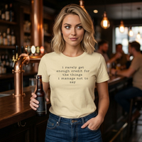 Load image into Gallery viewer, Woman in a modern lounge wearing the No 29 Unspoken Word side-seamed premium tee in cream, featuring charcoal minimalist typography.