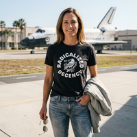 Load image into Gallery viewer, A woman on a NASA tarmac in front of a space shuttle wearing the No. 35 Radicalized By Basic Decency shirt in Vintage Black — white archival crow graphic and bold typography on premium dark canvas.