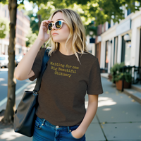 Load image into Gallery viewer, Someone in a curated urban streetscape wearing the No. 36 Big Beautiful Obituary shirt in Heather Brown — deadpan typewriter text on a breathable everyday uniform.