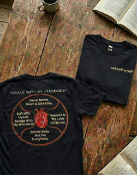 Load image into Gallery viewer, Flat lay on a rustic wooden table featuring two solid black No. 10 The Manifesto premium luxury tees, showcasing the front minimalist typography and the back anatomical heart graphic.