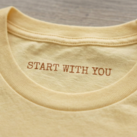 Load image into Gallery viewer, Macro shot of the internal collar showing the hidden "START WITH YOU" prompt on a premium luxury tee.