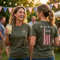 Load image into Gallery viewer, Two women in olive We The People premium tees showing the 1776 star circle chest graphic and We The People distressed American flag back print in an outdoor summer setting