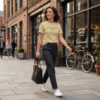 Load image into Gallery viewer, Woman walking past a coffee shop wearing the When God Made Me shirt in Soft Cream, front "When God Made Me, He..." text visible.