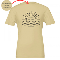 Load image into Gallery viewer, Soft Cream You Are The Light shirt, flat front view: a half sun rising over water with You Are The Light in serif inside the sun, and Matthew 5:14 below.
